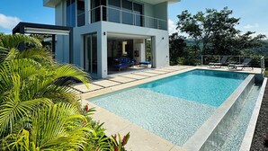 Ein modernes, zweistöckiges Haus mit großem Pool und üppiger Bepflanzung.