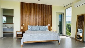 Ein modernes Schlafzimmer mit einem großen Bett, einem Holzkopfende und Blick ins Grüne durch eine Schiebetür.