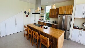 Eine moderne Küche mit einer zentralen Kochinsel, Holzstühlen, Edelstahlgeräten und Pendelleuchten.