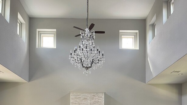 Un salon spacieux avec un haut plafond, un lustre, une cheminée, un téléviseur à écran plat et une grande fenêtre.