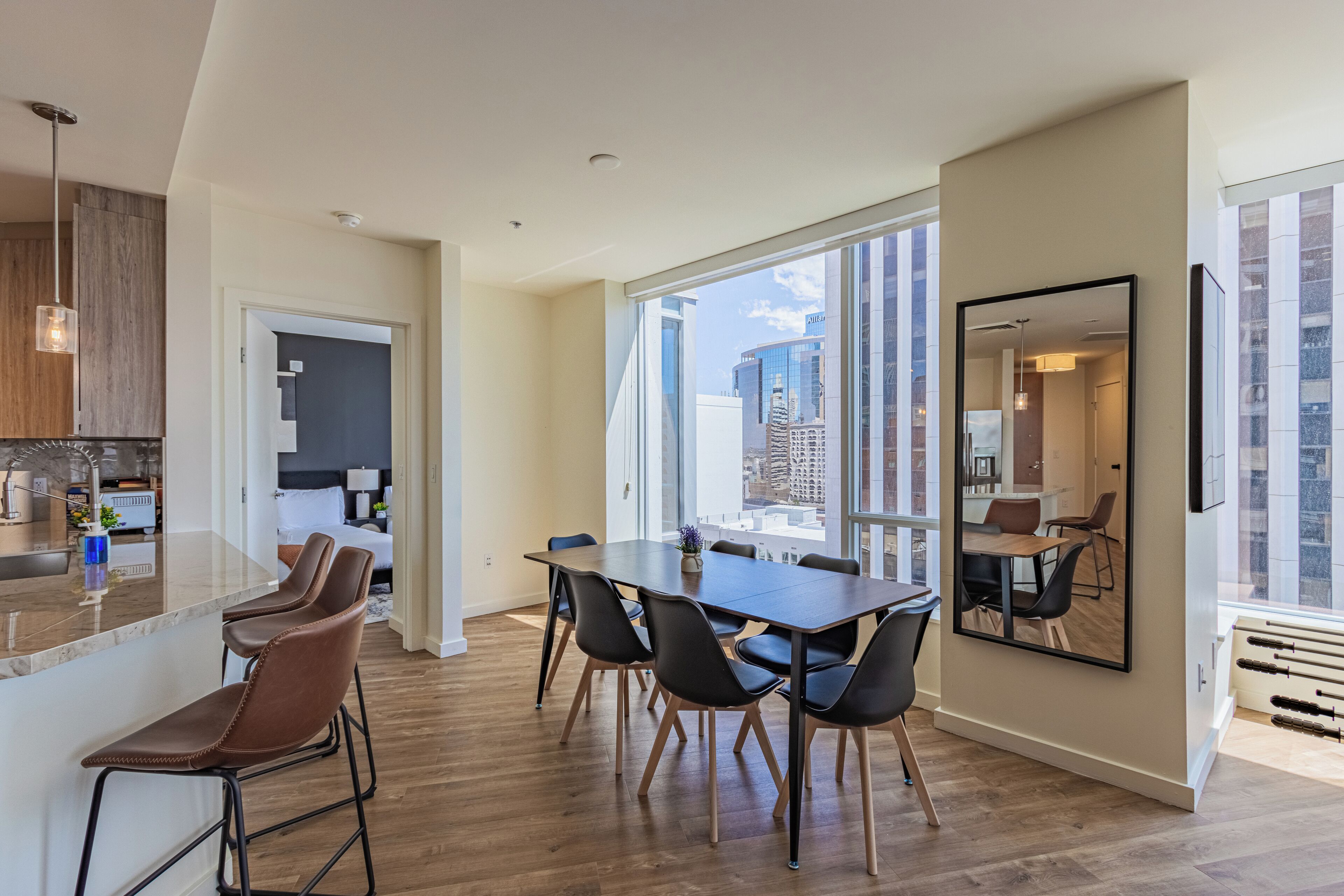 A modern kitchen with a large island, a dining area with a long table and chairs, and a large window offering a city view.