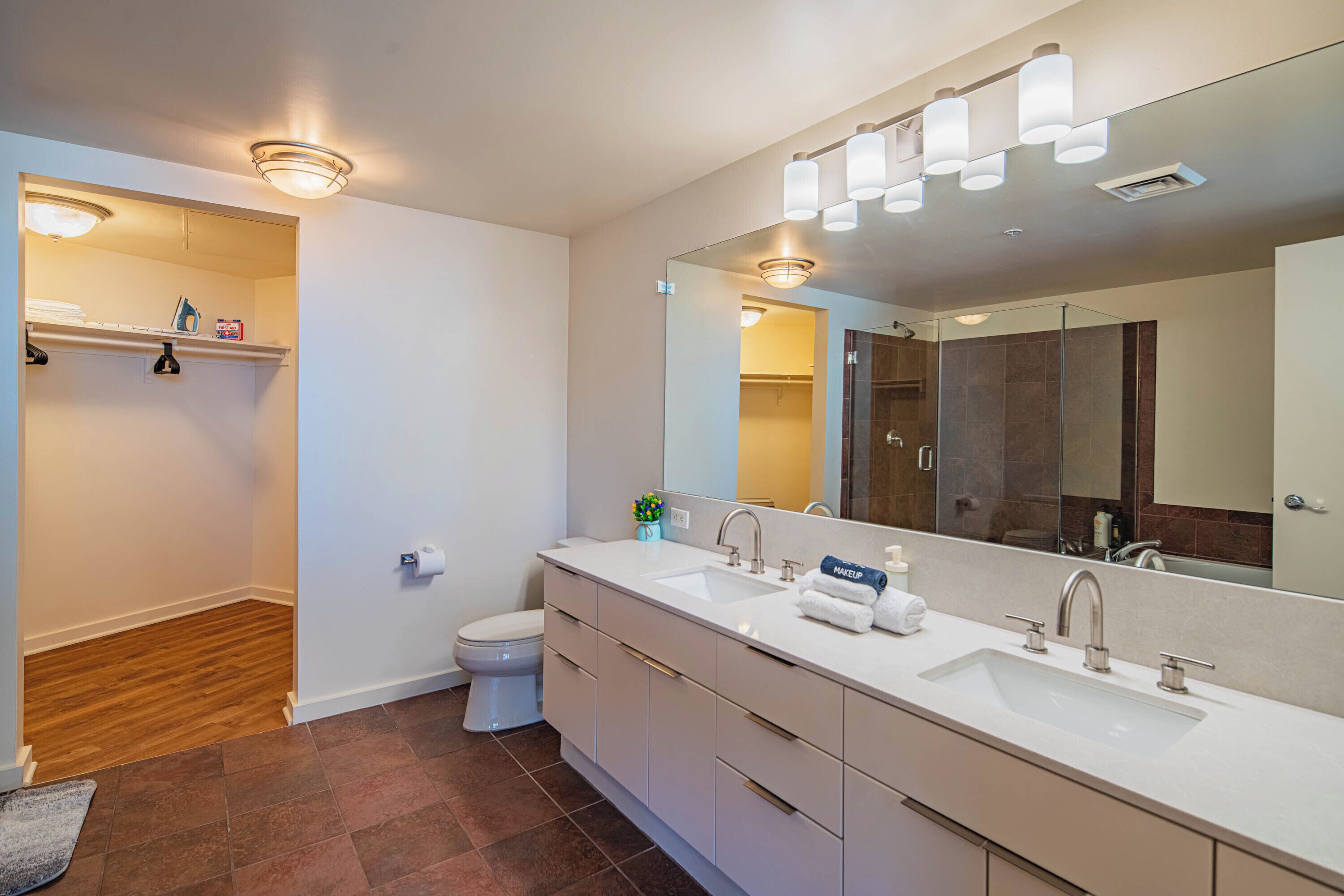 A modern bathroom with a large mirror, two sinks, and a toilet.