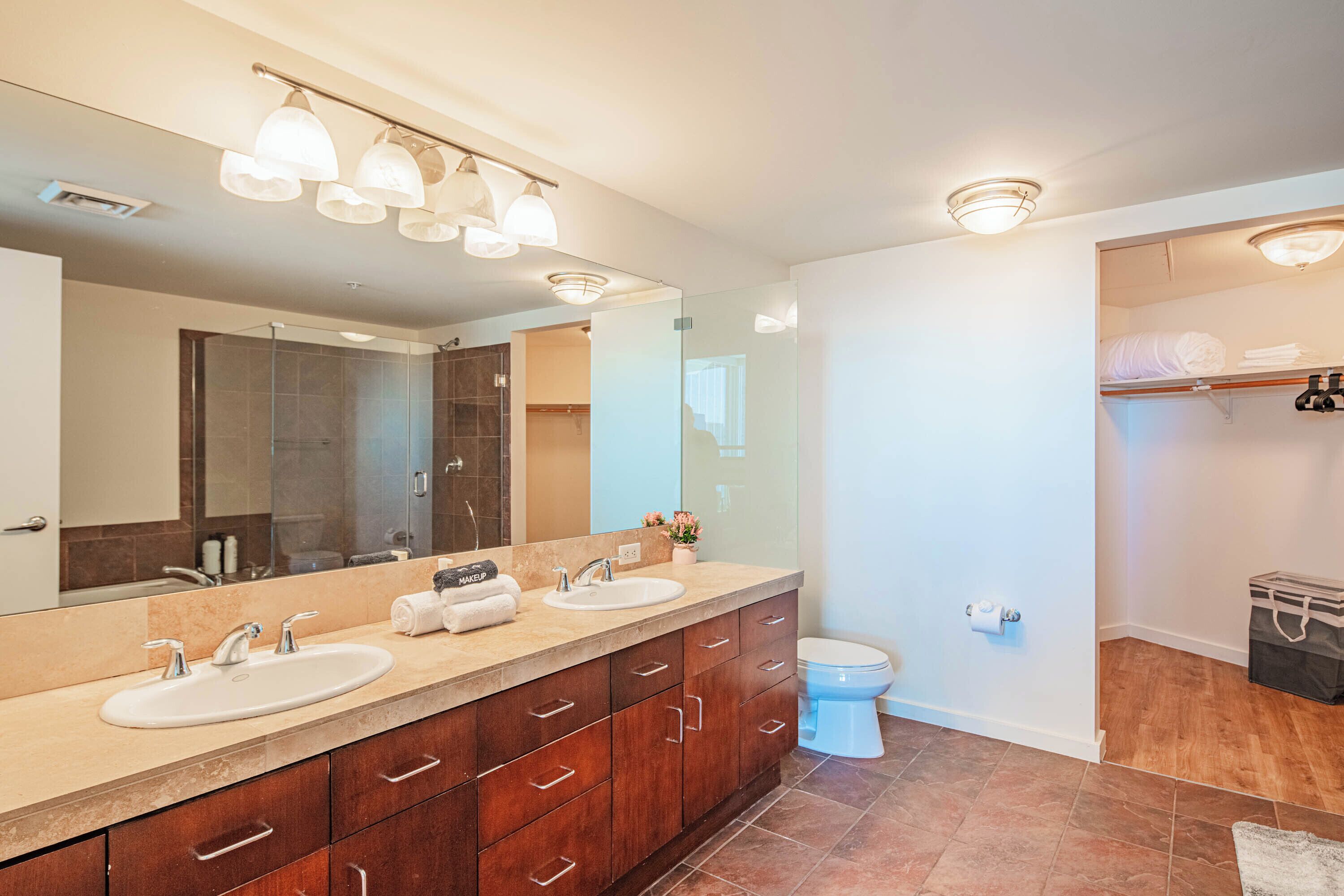 A modern bathroom with a large mirror, dual sinks, and a toilet.