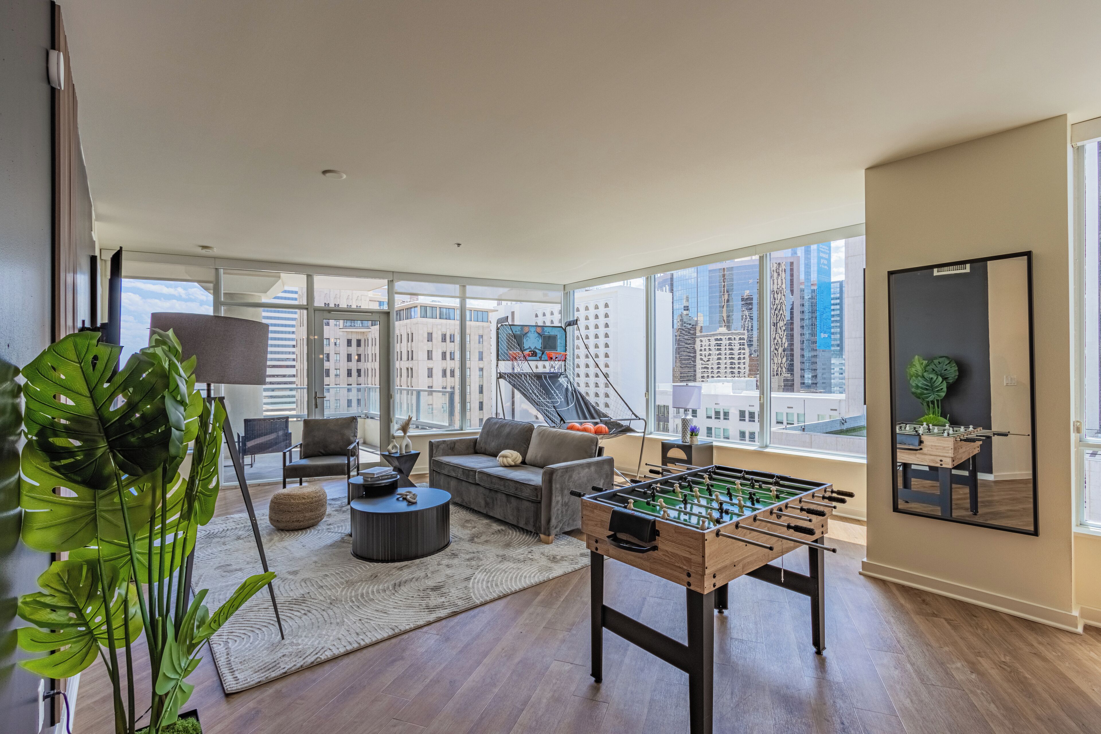 A modern living room with a foosball table, a sofa, and a coffee table. Large windows offer a view of the cityscape.