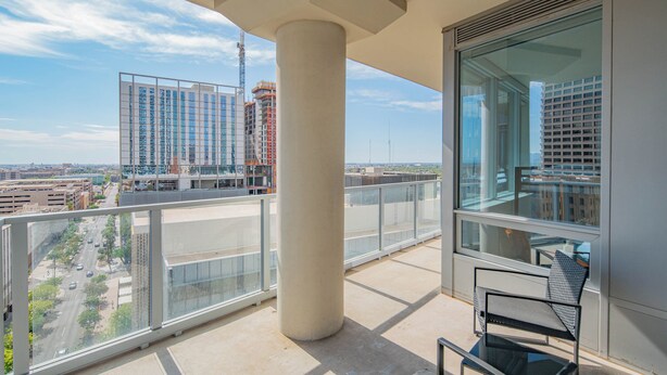 A balcony with a glass railing, a metal chair, and a view of a cityscape with buildings and a construction crane. - ROVE LIVING/KL - 44 Monroe (Phoenix)