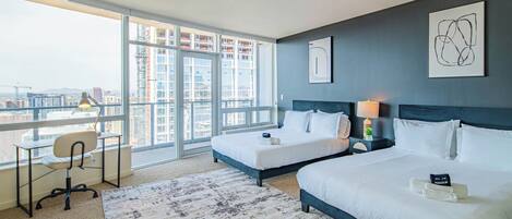 A modern hotel room with two beds, a desk, and a large window offering a city view.