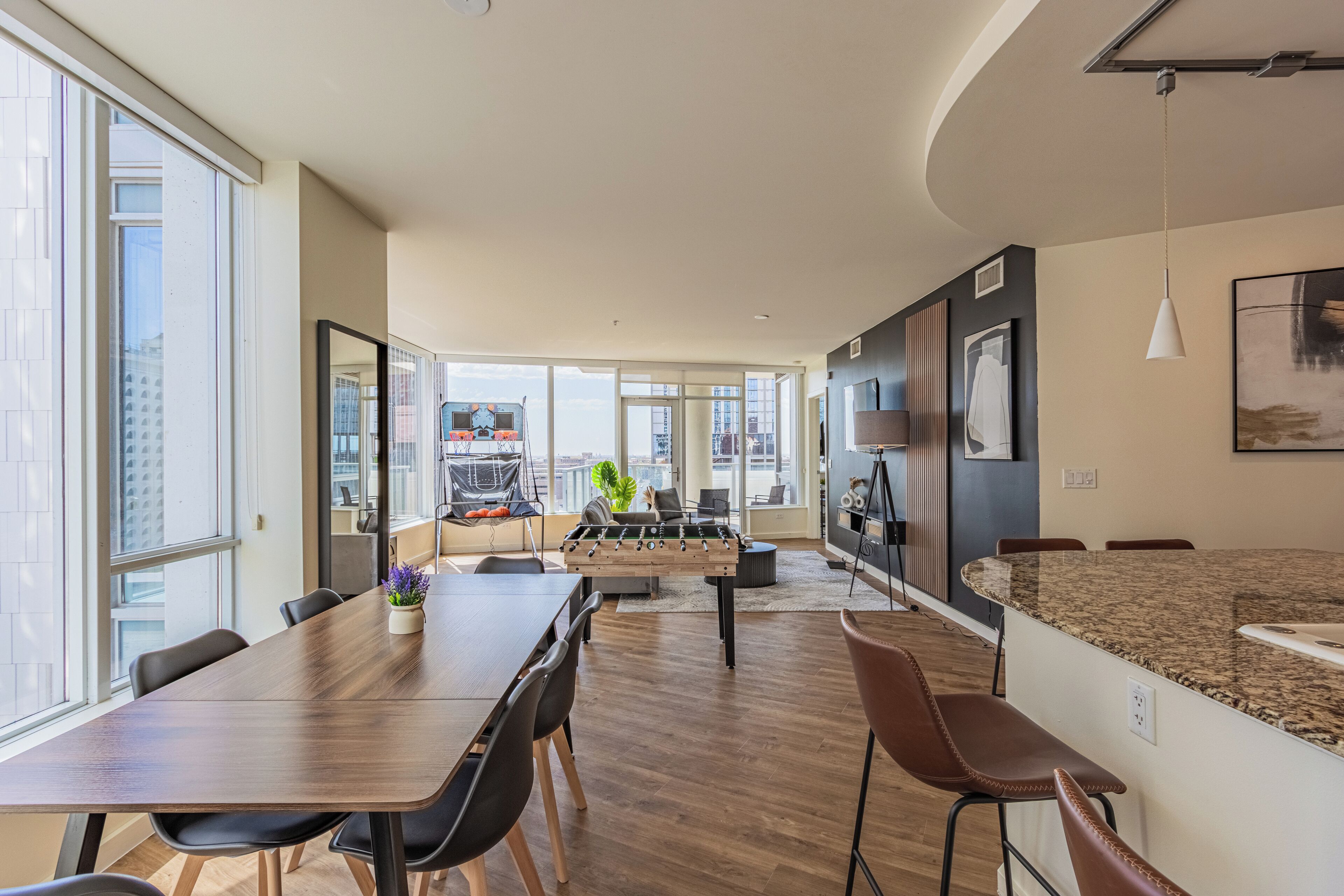 A modern kitchen with a foosball table, a dining area with a long table and chairs, and a kitchen island with seating.