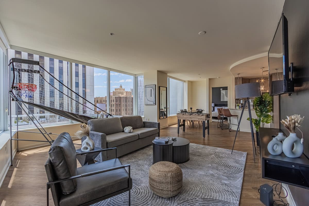 A spacious living area with a large window, a sofa, a coffee table, and a dining table with chairs.
