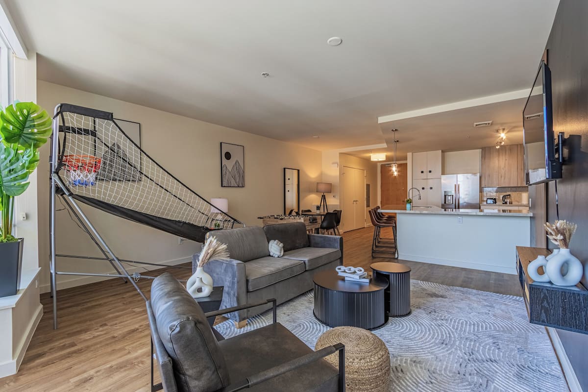 A modern living room with a grey sofa, a coffee table, and a staircase leading to a kitchen area.