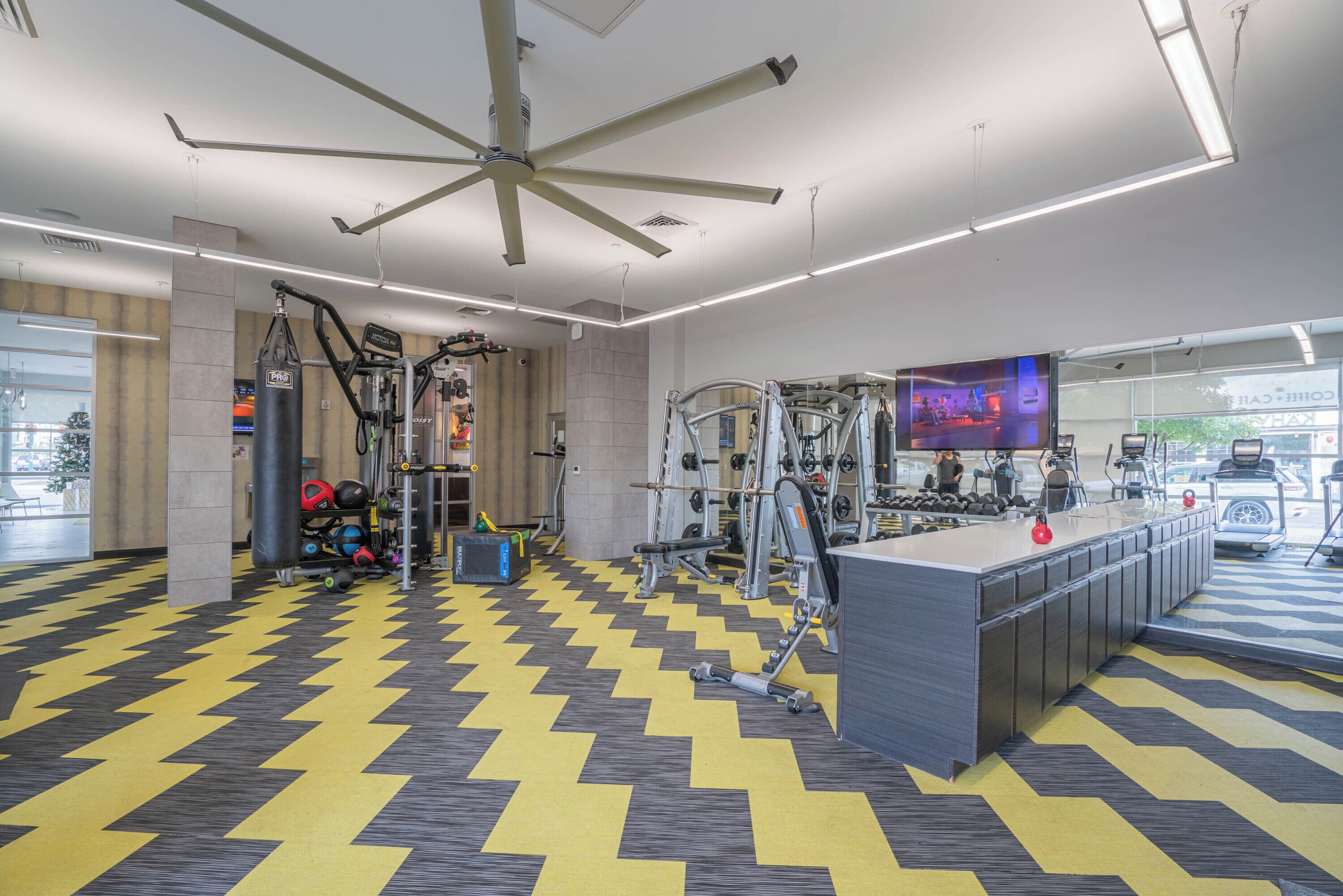Une salle de sport équipée de matériel d’exercice, dotée d’un ventilateur de plafond et d’un grand écran de télévision.