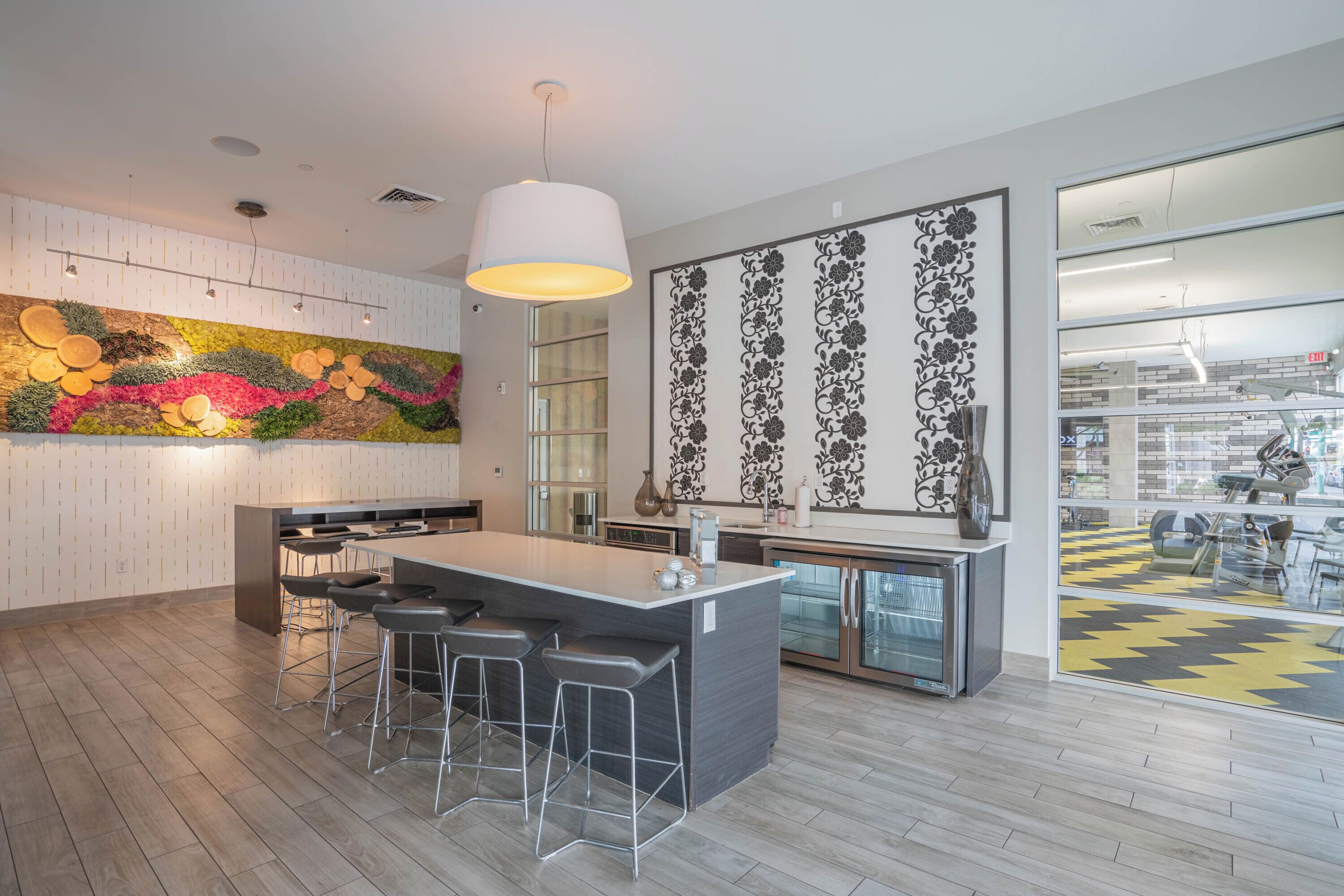 A modern kitchen with a central island, bar stools, a hanging light fixture, and decorative wall art.