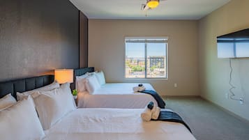 Habitación de hotel con dos camas, ventilador de techo, ventana con vistas a la ciudad y televisión montada en la pared.