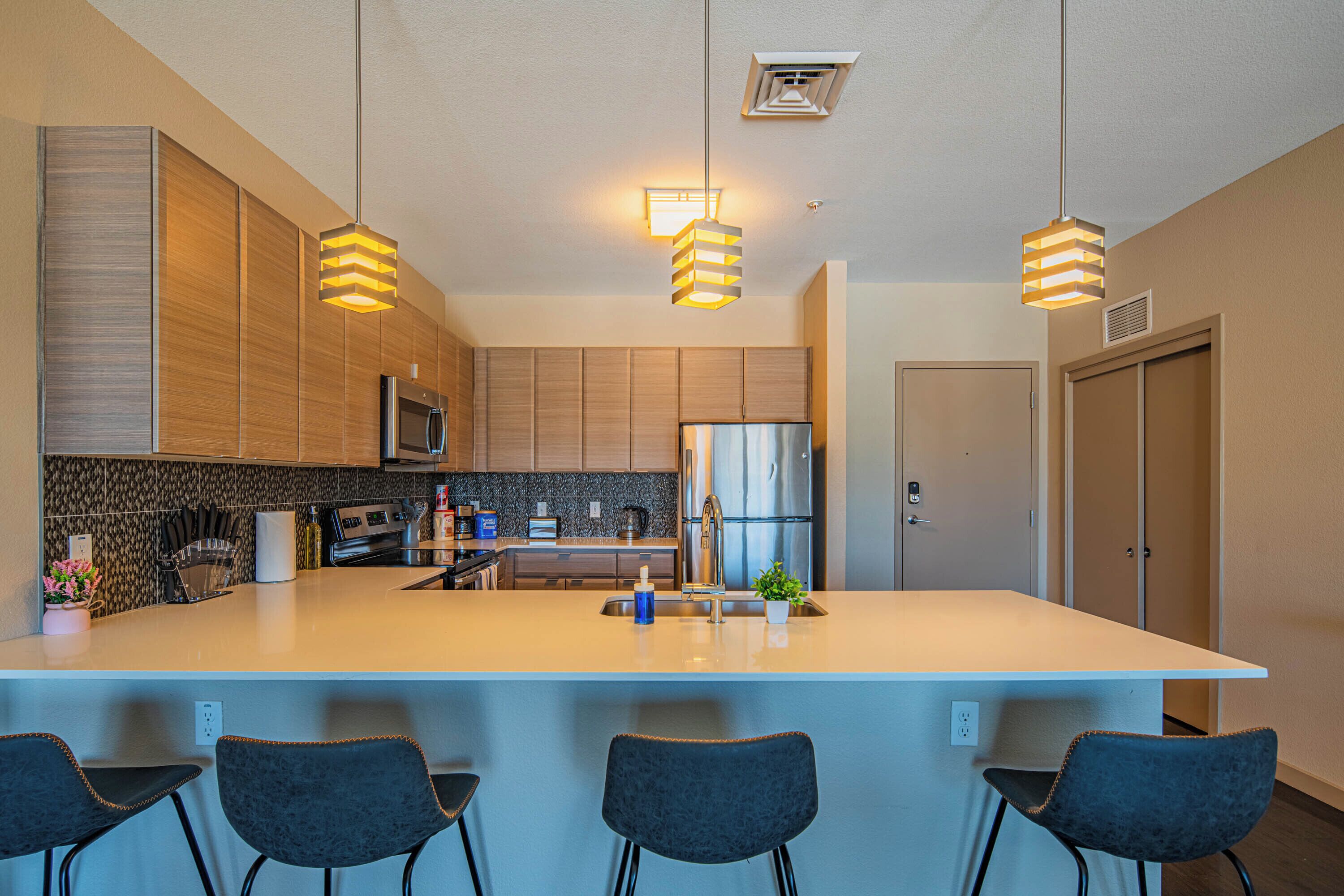 A modern kitchen with a large island, stainless steel appliances, and pendant lighting.