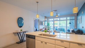 Une cuisine moderne dotée d’un grand îlot central, d’appareils électroménagers en acier inoxydable, de luminaires suspendus et offrant une vue sur l’extérieur.