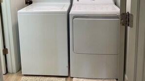 A laundry room with two white front-loading washers and dryers, wooden cabinets above, and a door to the left. - Cozy 3-bedroom garden level, dog friendly, in the heart of Greeley (Greeley)
