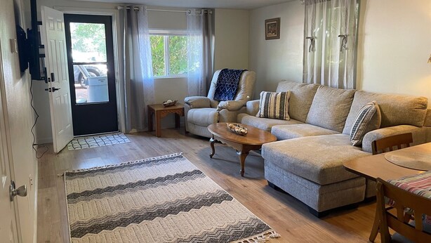 A living room with a sofa, coffee table, and a rug. There is a door leading outside, and a small table with a bowl on it. - Cozy 3-bedroom garden level, dog friendly, in the heart of Greeley (Greeley)
