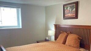 A neatly made bed with a wooden headboard, a bedside table with a lamp, and a window with blinds. - Cozy 3-bedroom garden level, dog friendly, in the heart of Greeley (Greeley)