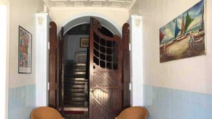 A hallway with a patterned floor, a wooden door, two wicker chairs, and a painting on the wall.
