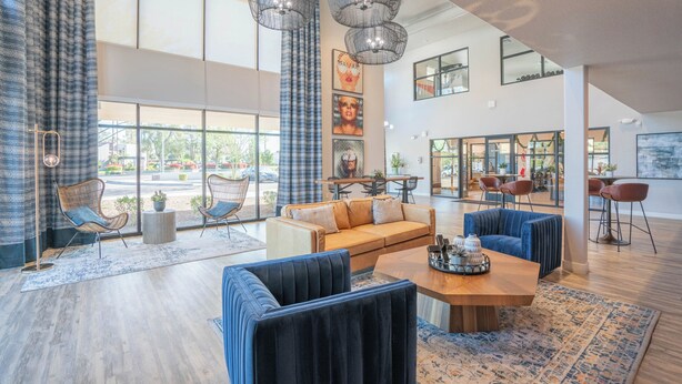 Eine großzügige Lobby mit modernem Design, ausgestattet mit einer großen Sitzecke, einem Holztisch und Blick ins Freie durch große Fenster.
