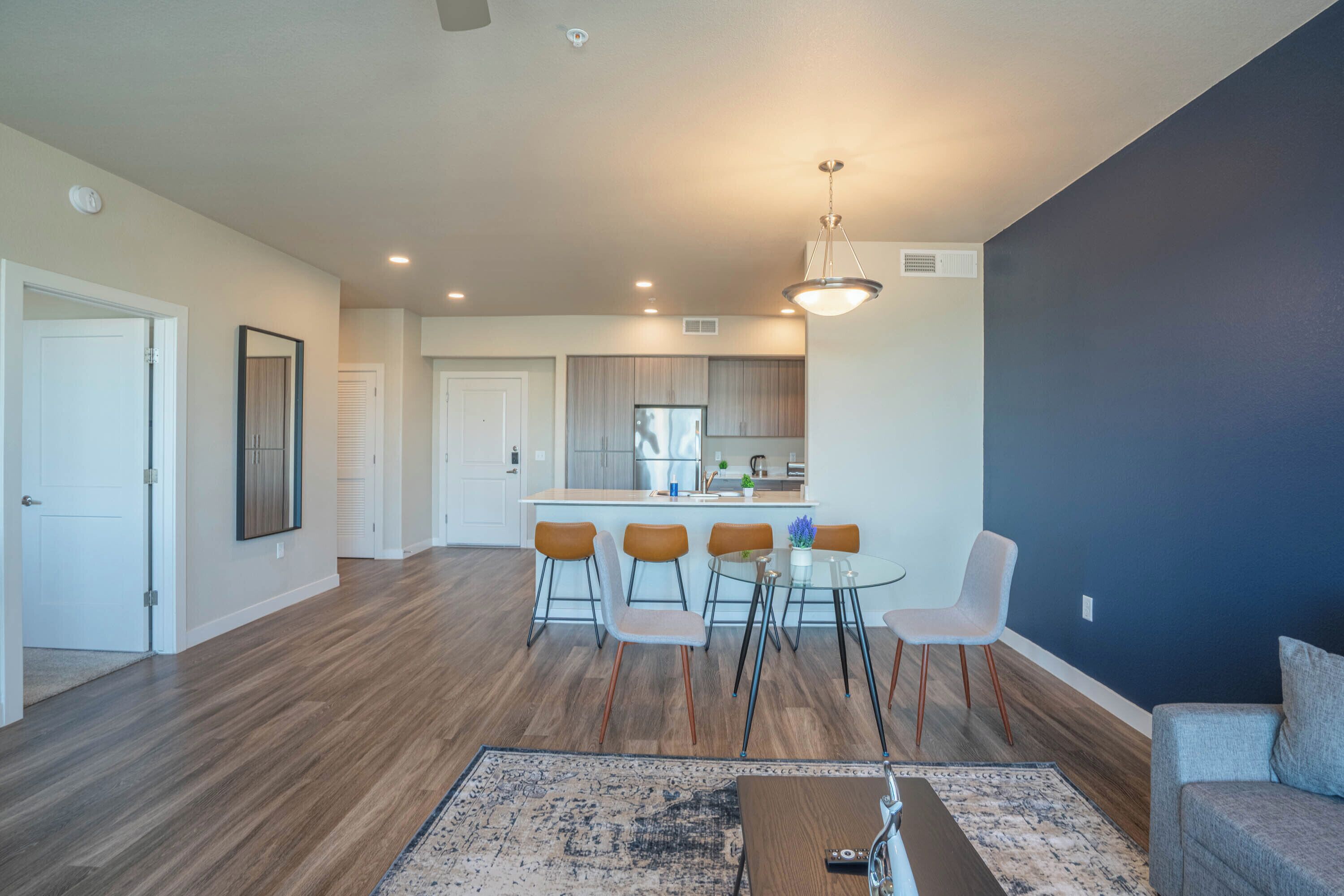 A modern living room with hardwood flooring, a glass dining table with five chairs, a sofa, and a coffee table.
