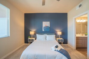 A hotel room with a large bed, two bedside tables with lamps, a painting on the wall, and a bathroom visible through an open door. - ROVE LIVING/KL - V on Broadway (Tempe)