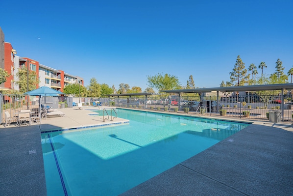 A swimming pool with clear blue water, surrounded by a fence, and adjacent to a building with balconies. - ROVE LIVING/KL - V on Broadway (Tempe)