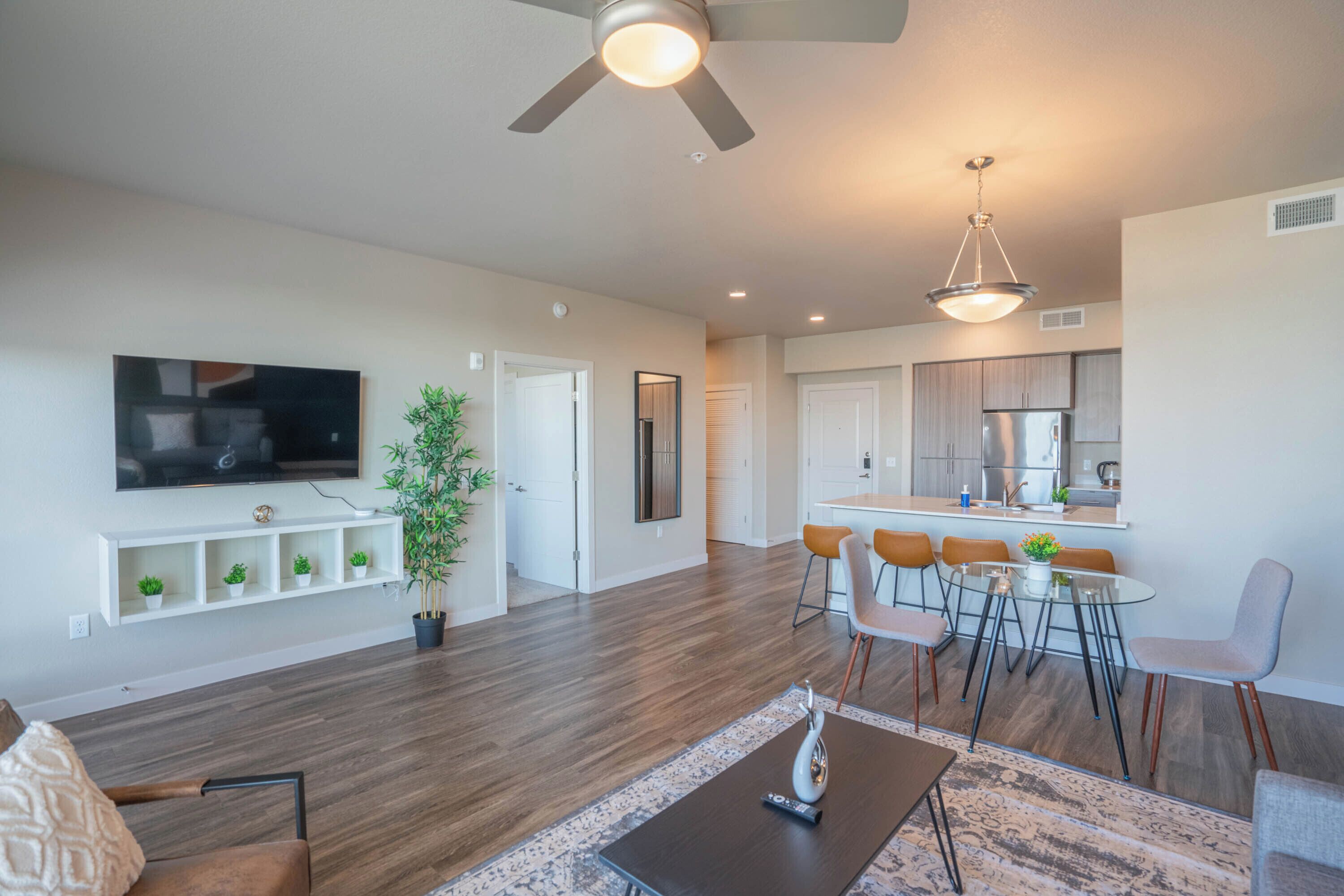 A modern living room with a flat-screen TV, a coffee table, and a dining area with a glass table and chairs.