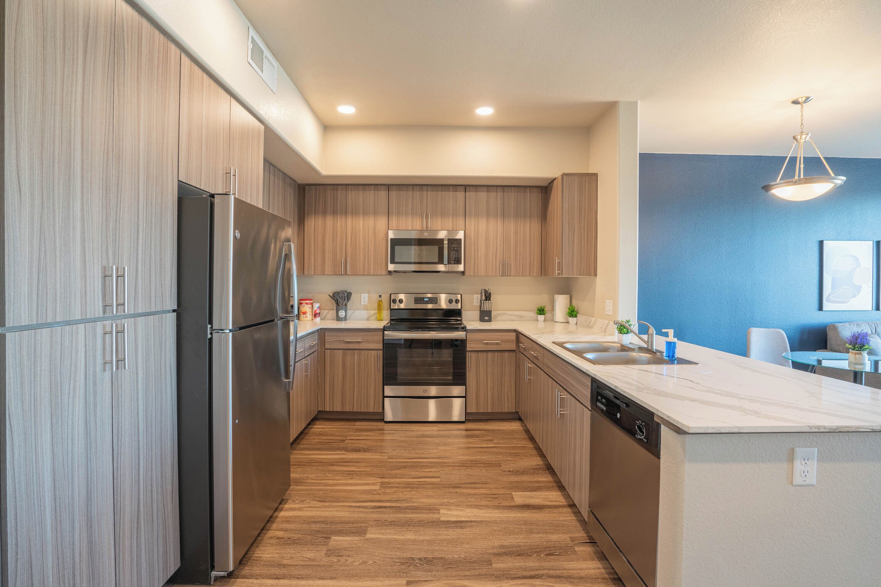 A modern kitchen with stainless steel appliances, wooden cabinets, and a marble countertop.
