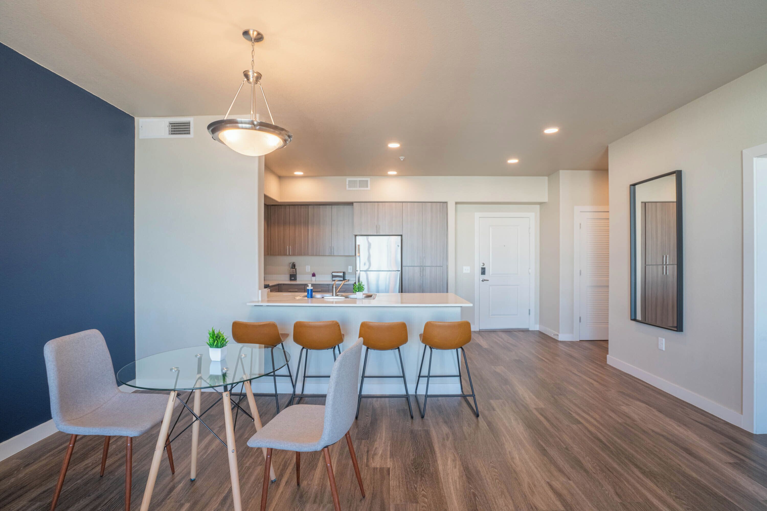 Una cocina moderna con una isla central, taburetes de bar y una mesa de comedor de vidrio.