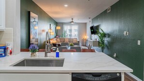 A kitchen with a dishwasher, a dining area with a table and chairs, a sofa, and a TV mounted on the wall. - ROVE LIVING/KL - The Fredrick Tempe (Tempe)