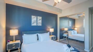 A hotel room with a large bed, two bedside tables with lamps, a ceiling fan, and a large mirror reflecting the room.