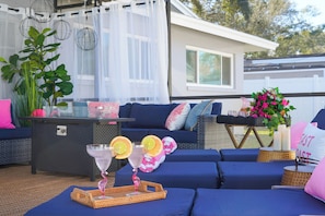 A patio area with blue cushioned seating, a wicker table with drinks, and a white house in the background. - Heated Pool + Hot Tub | 3 Kings | Near the Beach (Largo)