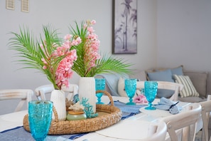 A dining table with a woven tray, a vase with pink flowers, and blue glassware. - Heated Pool + Hot Tub | 3 Kings | Near the Beach (Largo)