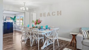 Un comedor con una mesa y sillas blancas, una araña y una pared con la palabra "BEACH" escrita.