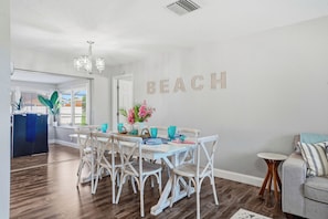 Un comedor con una mesa y sillas blancas, una araña y una pared con la palabra "BEACH" escrita.