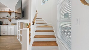 A staircase with wooden steps and white walls, leading to a landing with a TV and shelves. - The Lost Chancla - Pet Friendly! View of Community Pool! (Port Aransas)