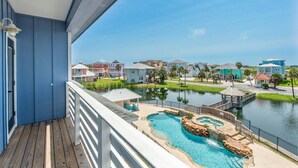 A balcony with a view of a swimming pool, a small dock, and a row of colorful houses. - The Lost Chancla - Pet Friendly! View of Community Pool! (Port Aransas)