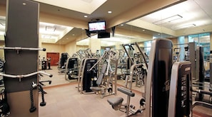 Un gimnasio con varias máquinas de ejercicio, una pantalla de televisión y un espejo que refleja el equipo.