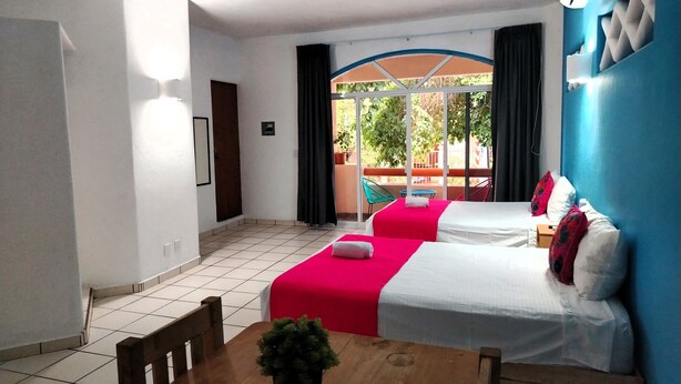 A hotel room with two beds, a dining table with a plant, a ceiling fan, and a view of greenery outside. - Casa Cacaluta (Santa María Huatulco)