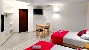 A hotel room with two beds, a desk, a chair, a TV, and a ceiling fan. - Casa Cacaluta (Santa María Huatulco)