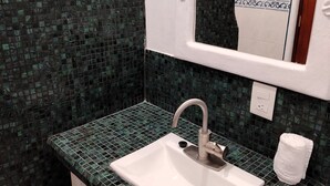 A bathroom with a white sink, green mosaic tiles, and a mirror with a wooden frame. - Casa Cacaluta (Santa María Huatulco)