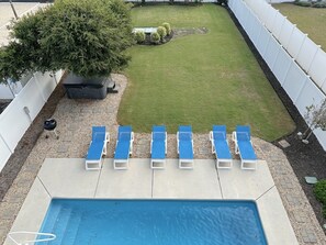 Un jardin avec une piscine, une pelouse et une rangée de chaises longues bleues.