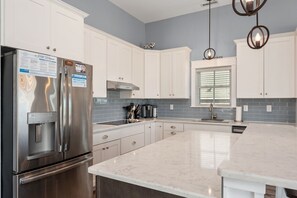 A modern kitchen with white cabinets, a stainless steel refrigerator, a built-in oven, and a large island with a sink.