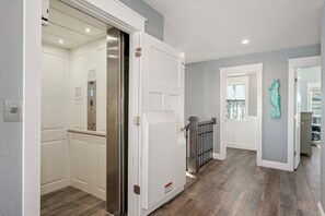 Corredor com elevador branco, porta decorada com um cavalo-marinho azul-turquesa e piso de madeira.