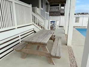 A wooden picnic table with benches, a white fence, and a pool in the background.