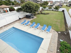 Un jardin avec une piscine, six chaises longues, un barbecue et une pelouse bien entretenue.