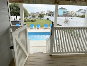 A wooden deck leading to a swimming pool with blue chairs and a white fence.