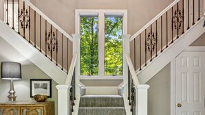 Una escalera con barandilla blanca, un mueble de madera con detalles decorativos y una puerta con picaporte de bronce.