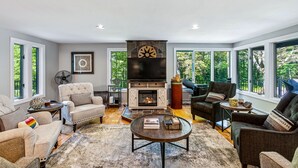 Un salón espacioso con chimenea, asientos cómodos y grandes ventanas que ofrecen vistas al exterior.