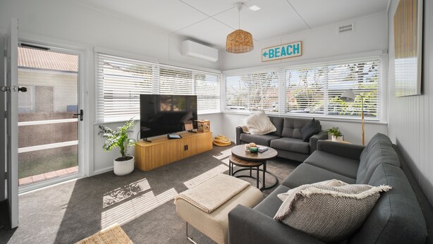 A modern living room with a grey sofa, a TV, and a sign indicating a beach direction. - Summer Breeze Forster
The Perfect Family Getaway on the Mid North Coast of NSW (Forster)